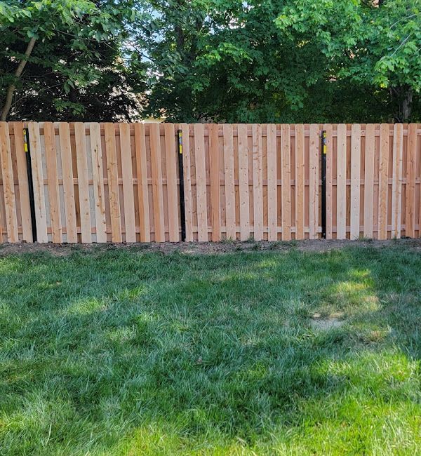 A wooden fence is in the middle of a lush green yard.