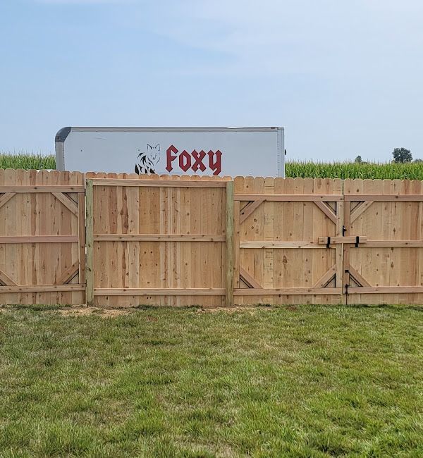 A wooden fence in a grassy field with a foxy truck in the background.