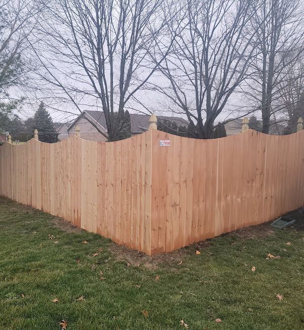 A wooden fence is surrounded by grass and trees in a backyard.