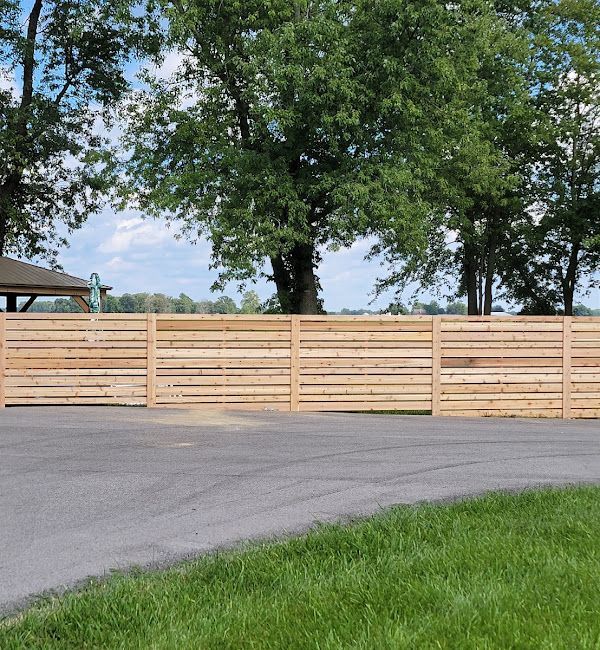 A wooden fence along a road with trees in the background