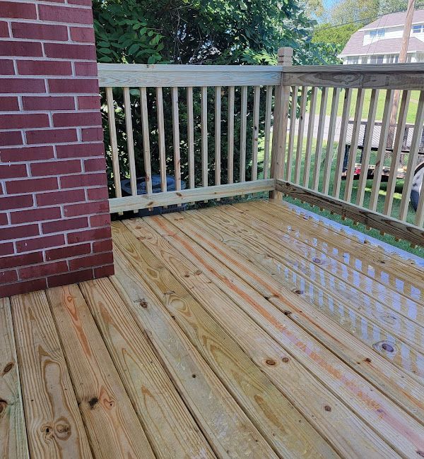 A wooden deck with a railing and a brick wall in the background.