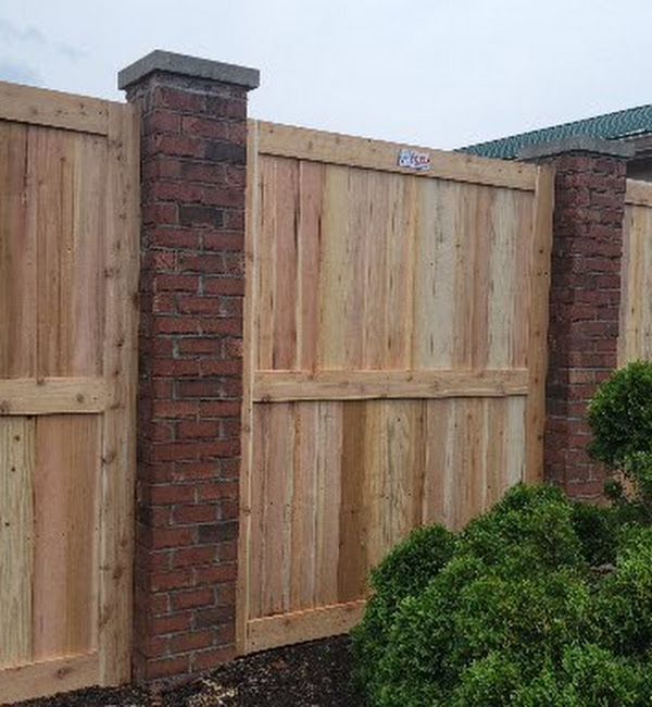 A wooden fence is surrounded by brick pillars and bushes.