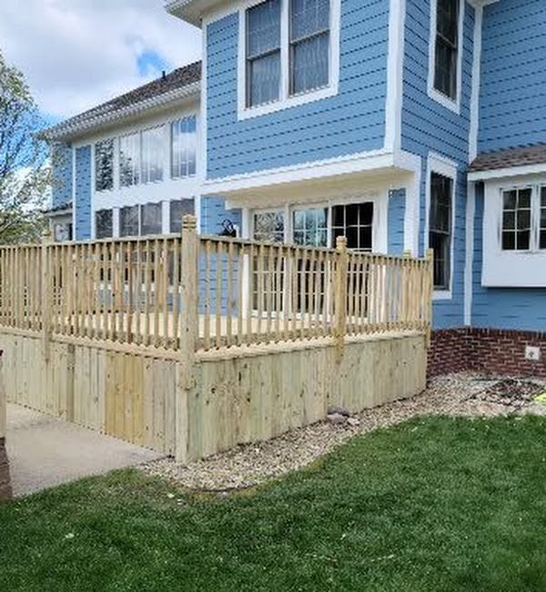 A blue house with a wooden deck in front of it.