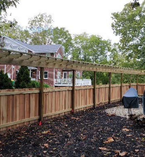A wooden fence with a pergola in the backyard of a house.