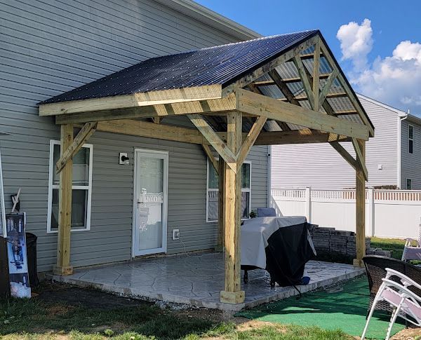 A wooden pavilion is being built in the backyard of a house.