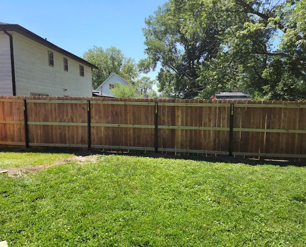 A wooden fence surrounds a lush green yard in front of a house.