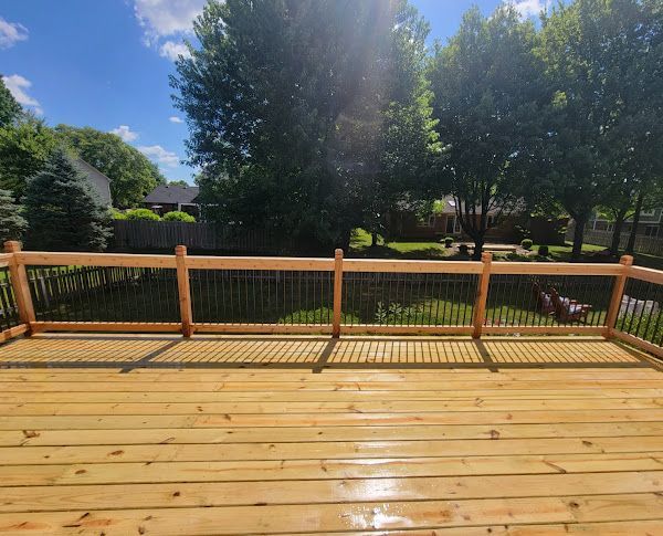 A wooden deck with a metal railing and trees in the background.
