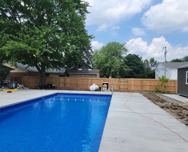A large swimming pool is surrounded by a wooden fence in a backyard.