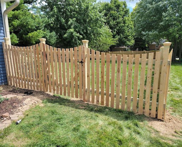 A wooden picket fence with a gate in a backyard.