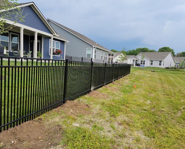 A black fence surrounds a lush green field in front of a house.