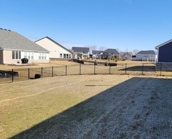 A fenced in yard with a lot of grass and houses in the background.