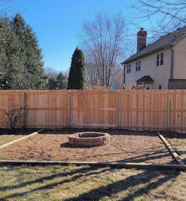 A wooden fence surrounds a fire pit in a backyard.