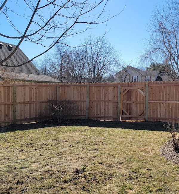 A wooden fence with a gate in the middle of a grassy yard.
