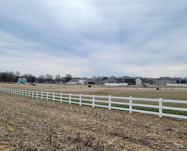 A white fence surrounds a field with houses in the background.