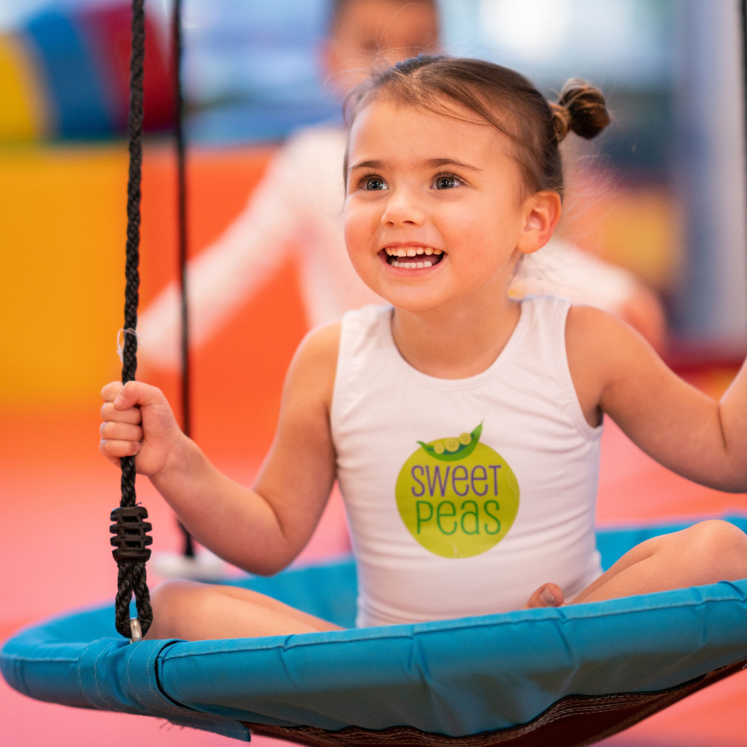 A little girl wearing a shirt that says sweet peas is sitting on a swing