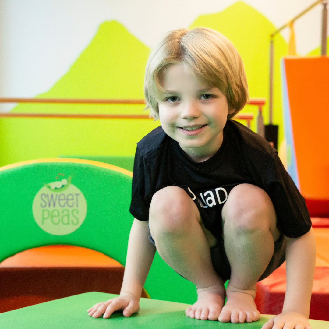 A young boy squatting on a green mat with sweet peas on it