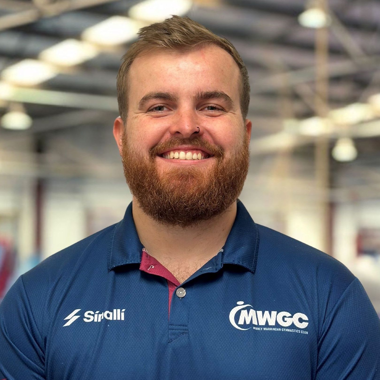 A man with a beard is wearing a blue shirt and smiling.