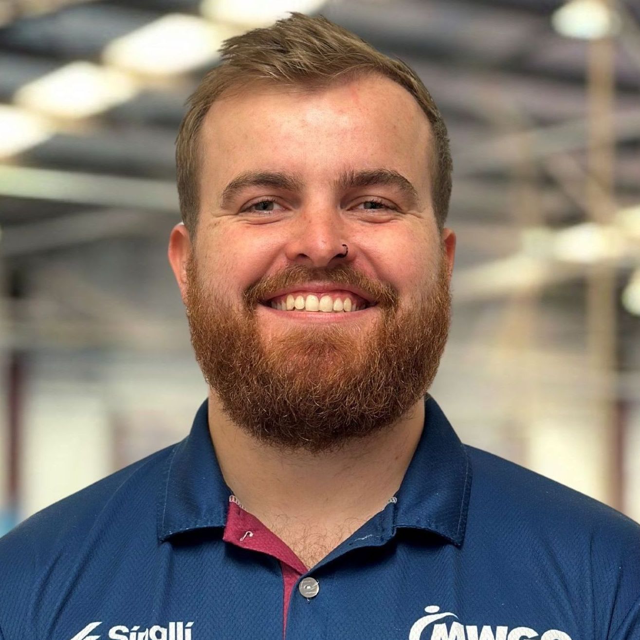 A man with a beard is wearing a blue shirt and smiling.