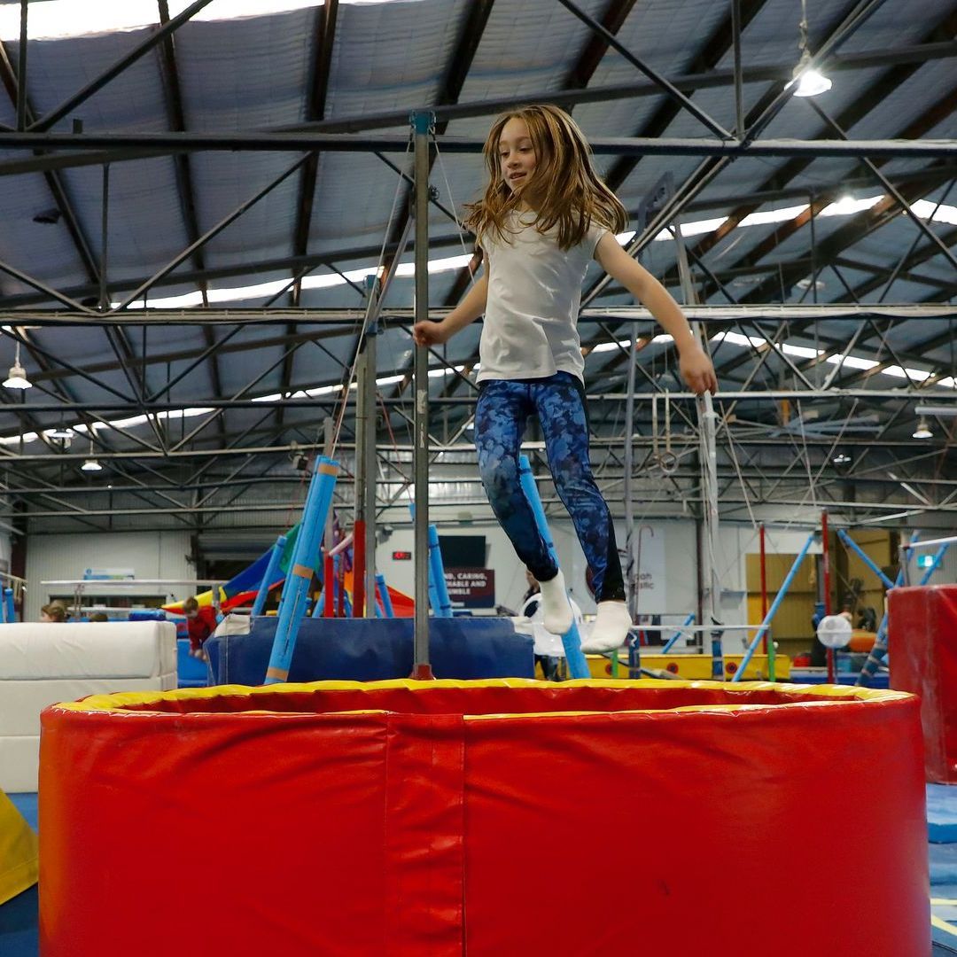 A little girl is jumping on a red trampoline
