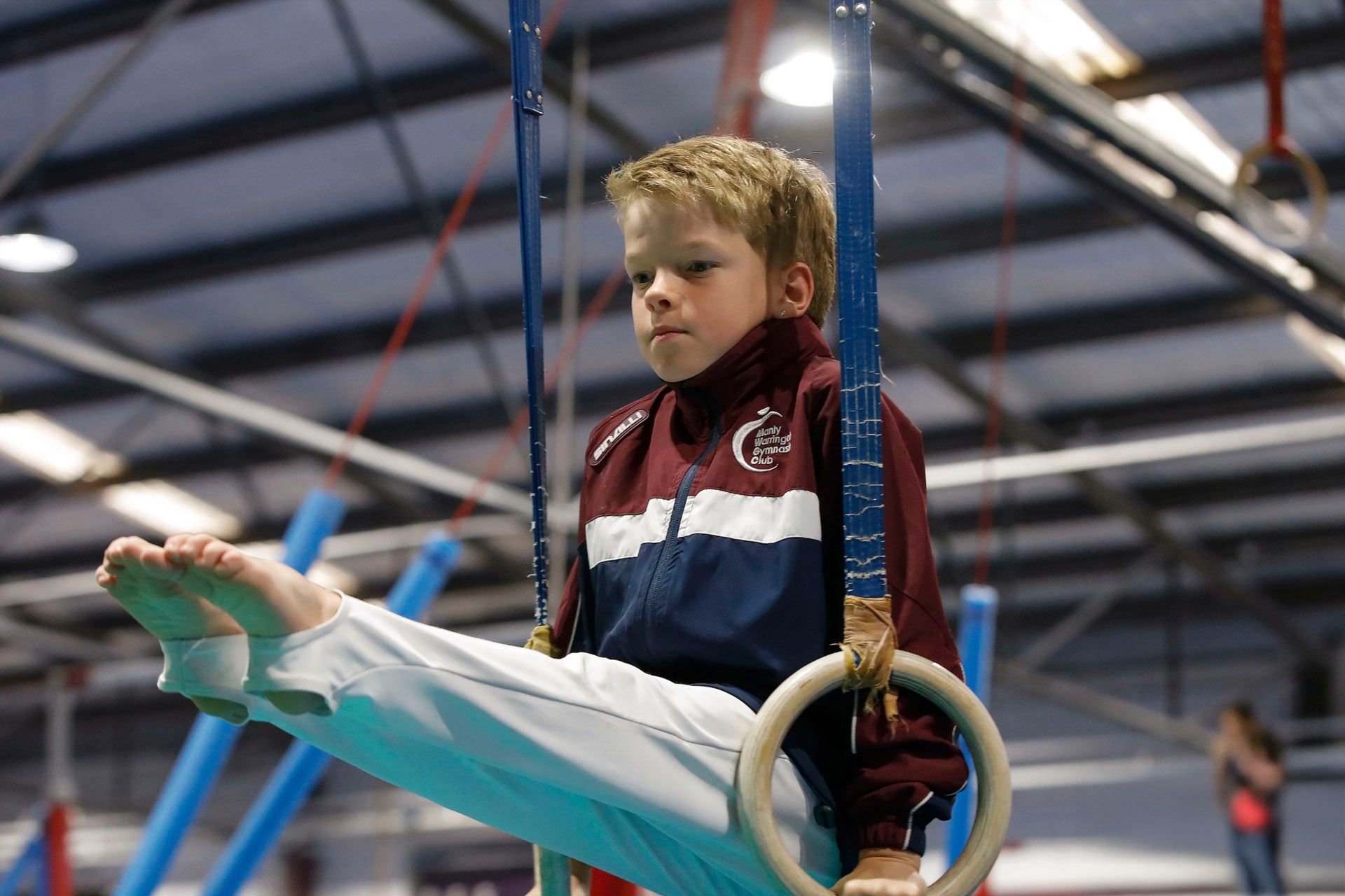 A young boy is sitting on a pair of gymnastic rings.