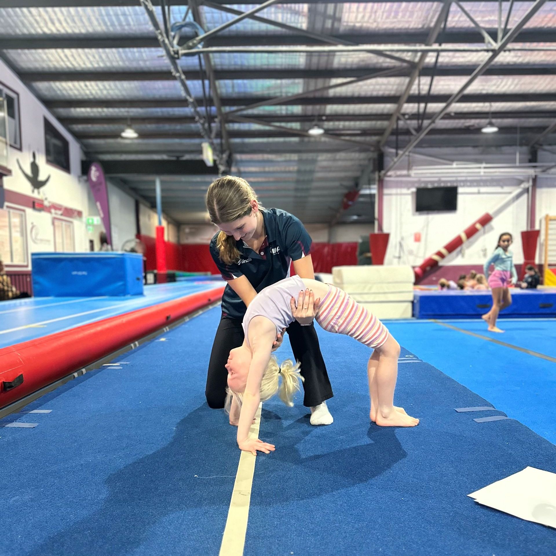 A woman is helping a little girl do a handstand in a gym.