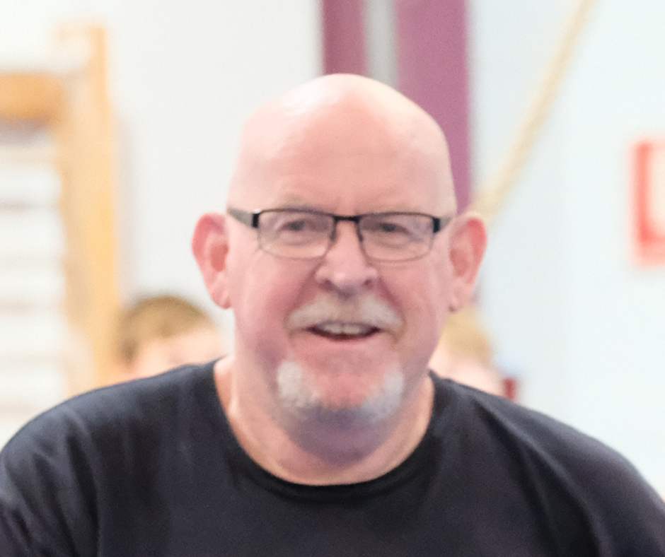 A bald man wearing glasses and a black shirt smiles for the camera