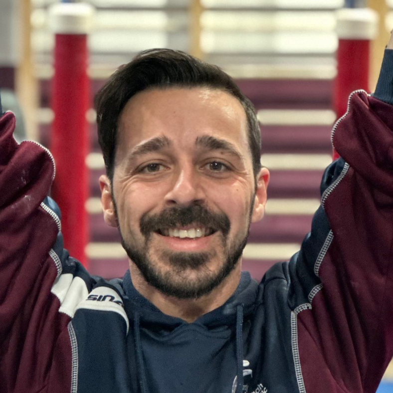 A man with a beard is smiling with his arms in the air.