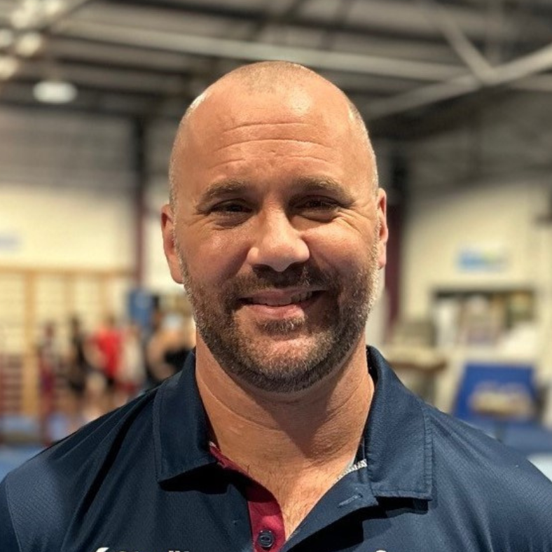 A bald man with a beard is smiling for the camera in a gym.