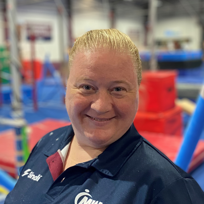 A woman in a blue shirt is smiling in a gym.