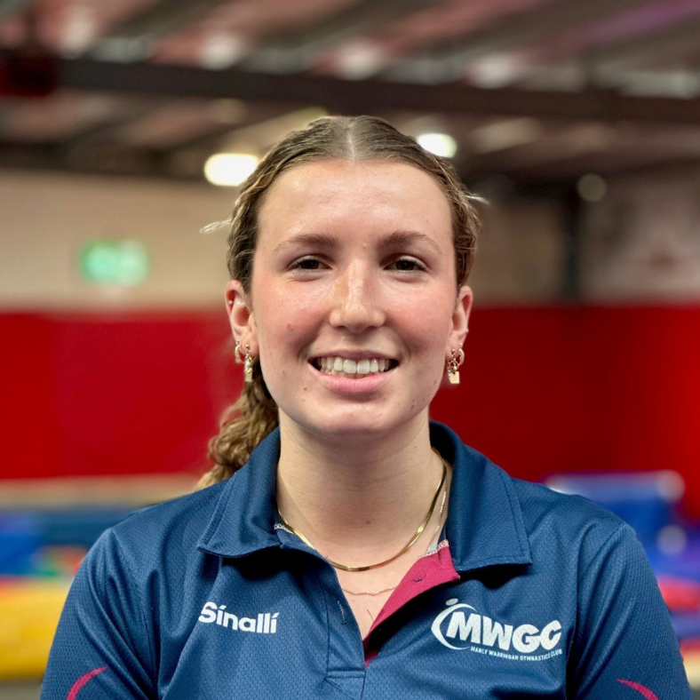 A woman in a blue shirt is smiling for the camera in a gym.