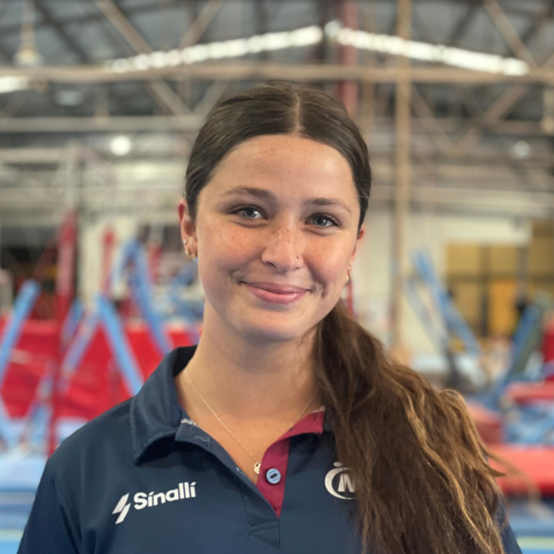 A woman wearing a blue shirt with the word sinalli on it is smiling in a gym.