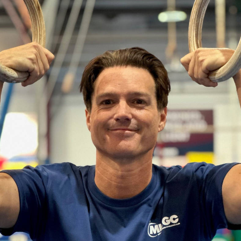 A man in a blue shirt is holding gymnastic rings over his head