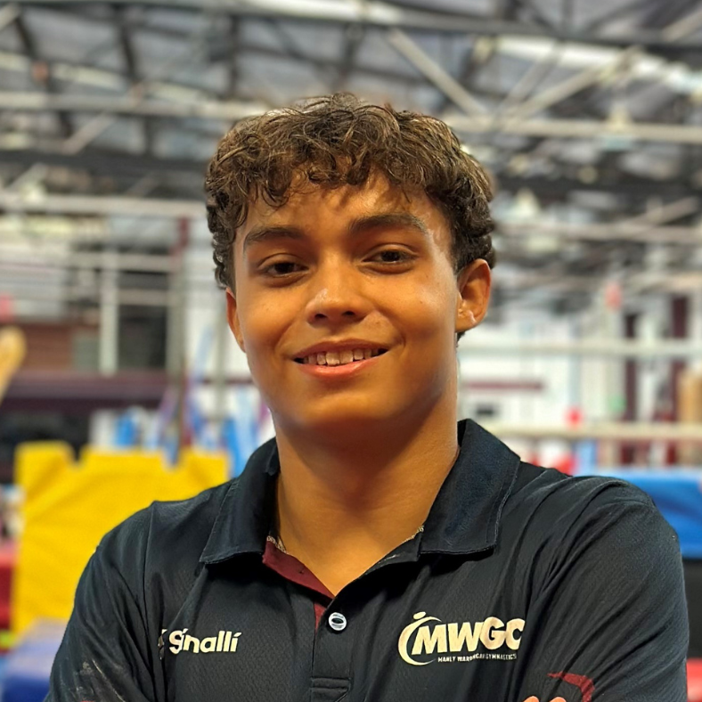A young man in a blue shirt is smiling for the camera in a gym.