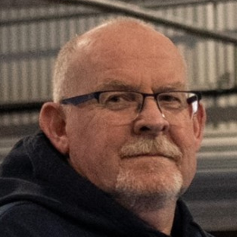 A bald man with glasses and a beard is wearing a black hoodie.