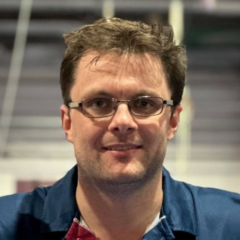 A man wearing glasses and a blue shirt smiles for the camera