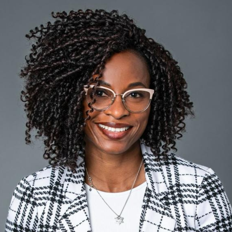 A woman with curly hair is wearing glasses and a plaid jacket.