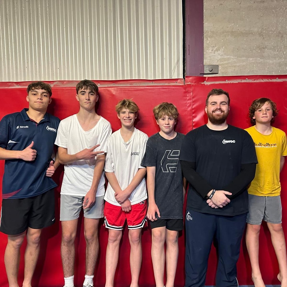 A group of young men are posing for a picture in front of a red wall.