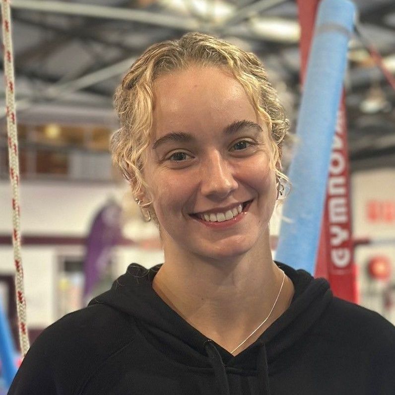 A woman in a blue shirt is smiling for the camera in a gym.