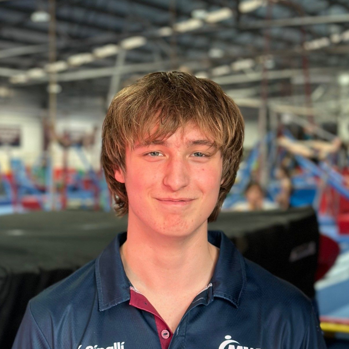 Young person in gymnastics apparel smiles in a gym setting.