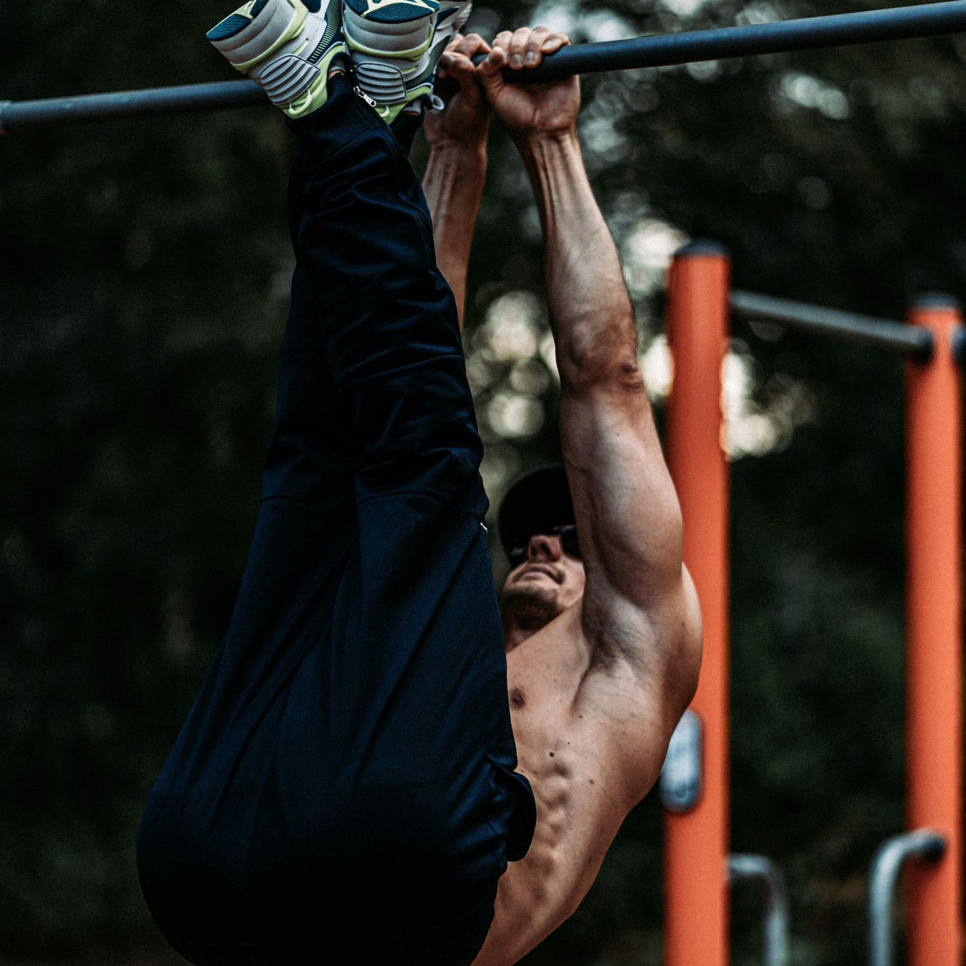 A shirtless man is doing a handstand on a bar.