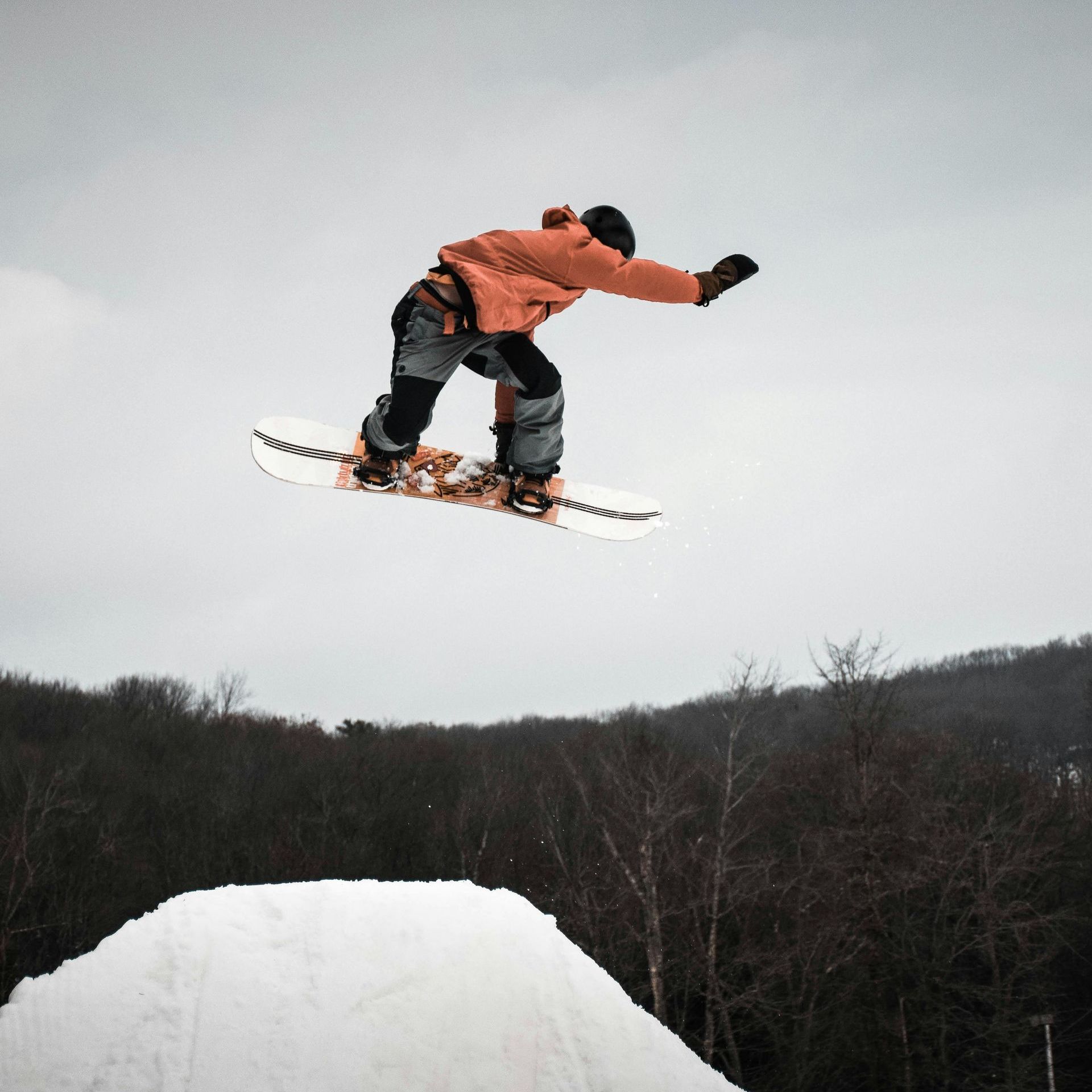 A snowboarder is jumping over a snowy hill