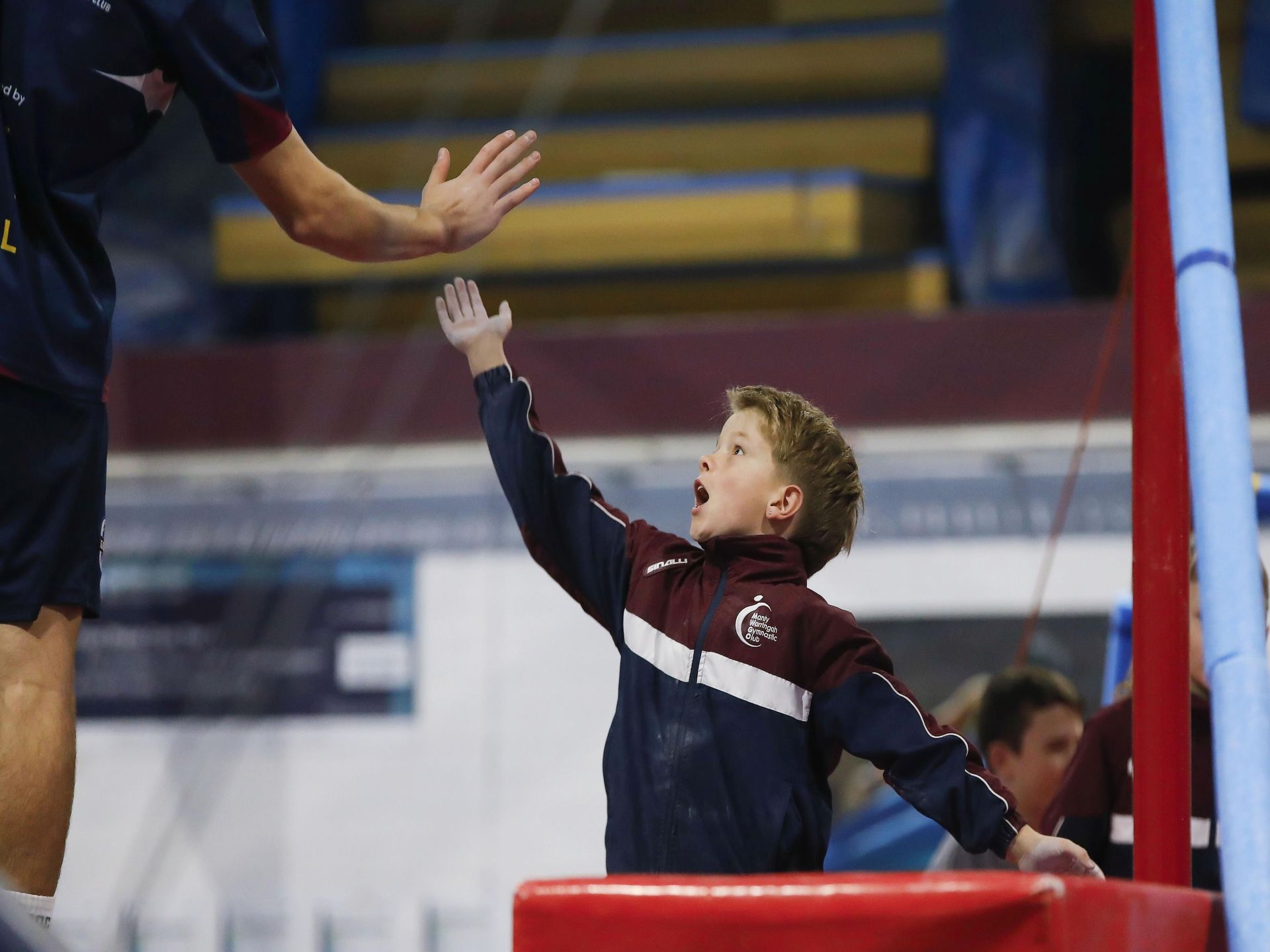 A young boy is reaching up to a man 's hand in a gym