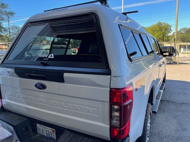 White Ford Super Duty truck with a camper shell, parked outside on a sunny day.