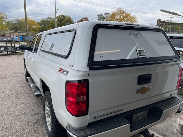 White Chevy Silverado pickup truck with a white camper shell in an outdoor setting.