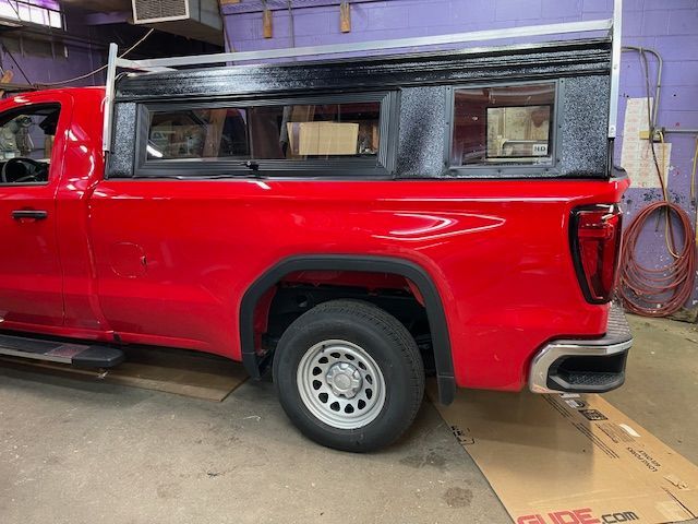 Red pickup truck with custom black and silver truck bed cover in a shop.