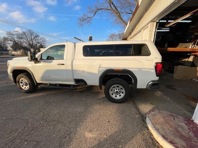 White pickup truck with a camper shell parked near a building on a sunny day.