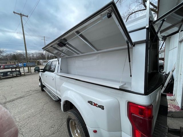 White pickup truck with white canopy, open, showing interior. Outdoors, overcast sky.