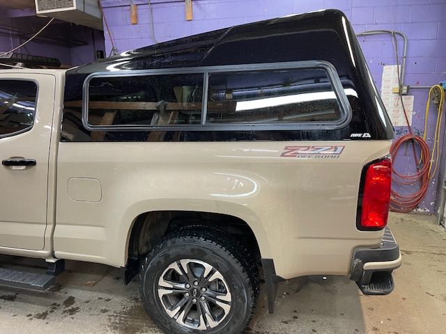 Tan pickup truck with a black camper shell. Side view.