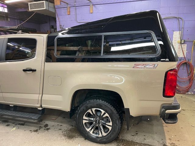 Tan pickup truck with black camper shell, parked inside a workshop.