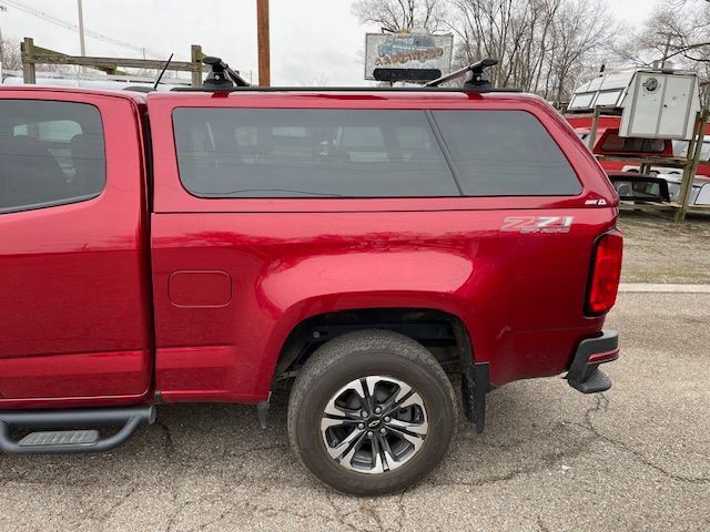 Red pickup truck with a camper shell and roof rack, parked outside.